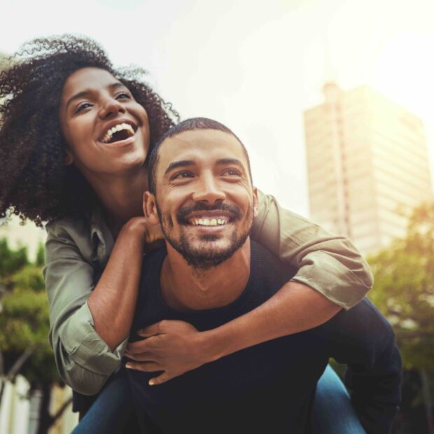 Cheerful young man giving piggyback ride to his girlfriend outdoors in the city