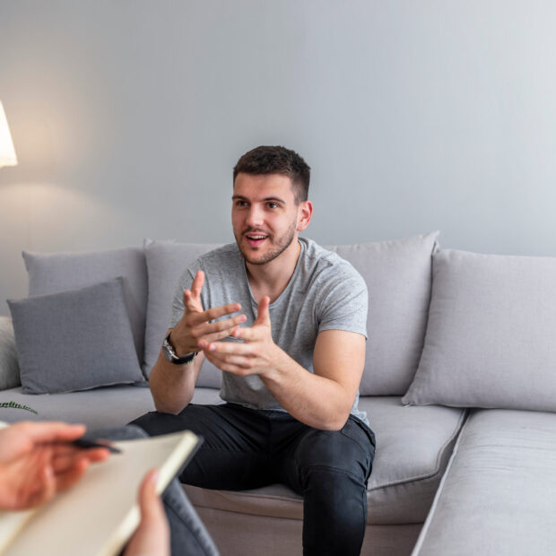 Psychologist talking with happy man in the office. Image of young man during psychological therapy. Female psychologist consulting man during psychological therapy session