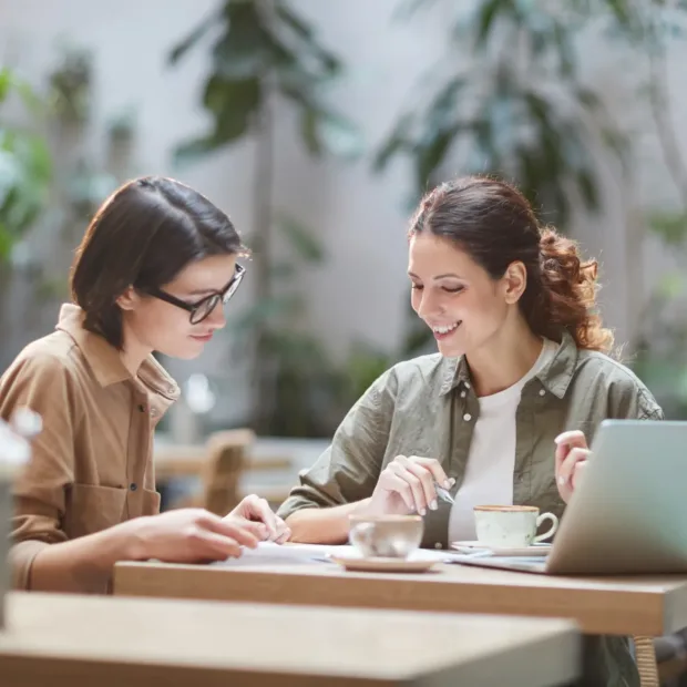 Portrait of two cheerful young omen enjoying work in beautiful outdoor cafe, copy space